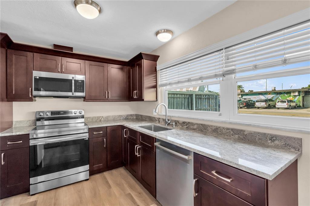 A kitchen with dark wood cabinets, stainless steel appliances, and granite countertops under a window — 6860 PARK STREET S, SOUTH PASADENA, FL