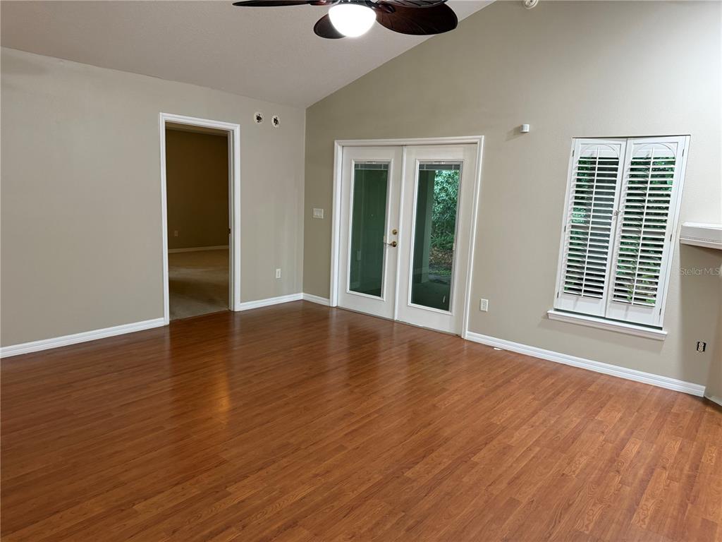 A living room features wood-look flooring, a vaulted ceiling, French doors, and plantation shutters — 731 SE 30TH AVENUE, OCALA, FL