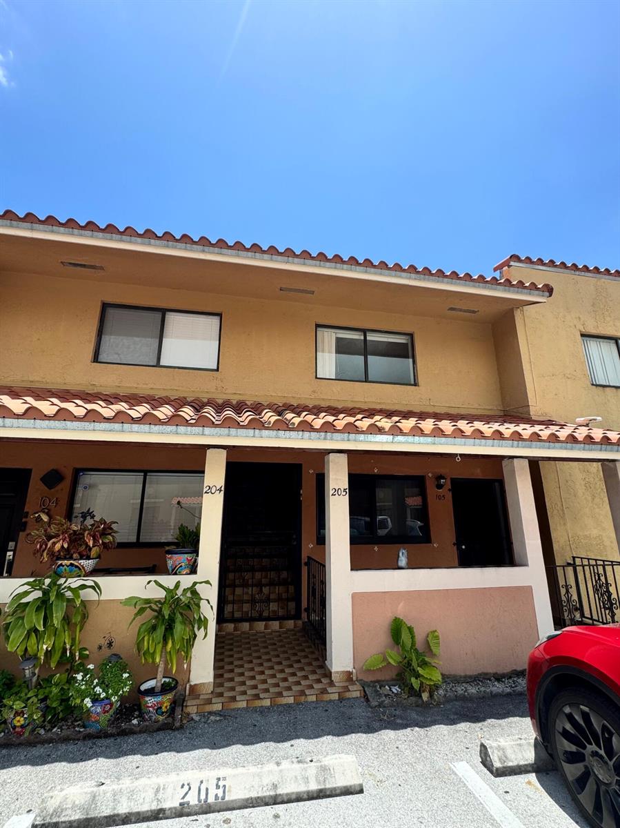The exterior of a two-story apartment building features tan stucco walls and a tiled roof — 2710 W 60th Place # 205, Hialeah FL 33016, HIALEAH, FL