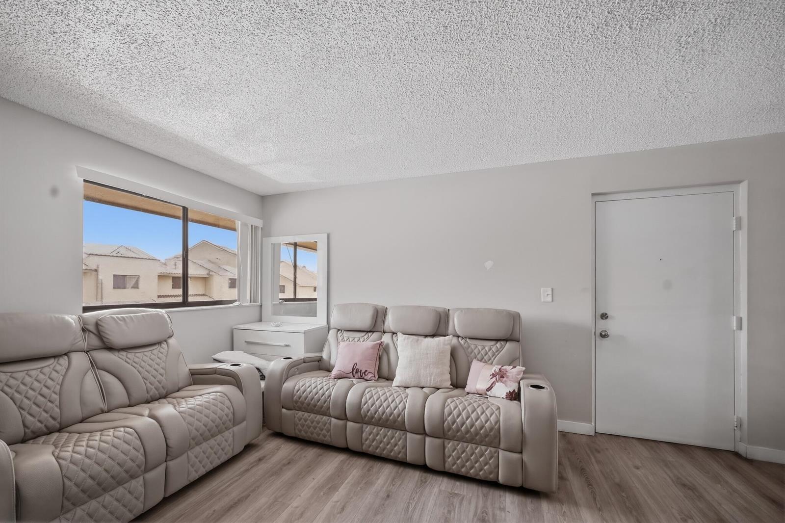 A living room with light gray walls, wood-look flooring, and two beige leather reclining sofas — 2710 W 60th Place # 205, Hialeah FL 33016, HIALEAH, FL