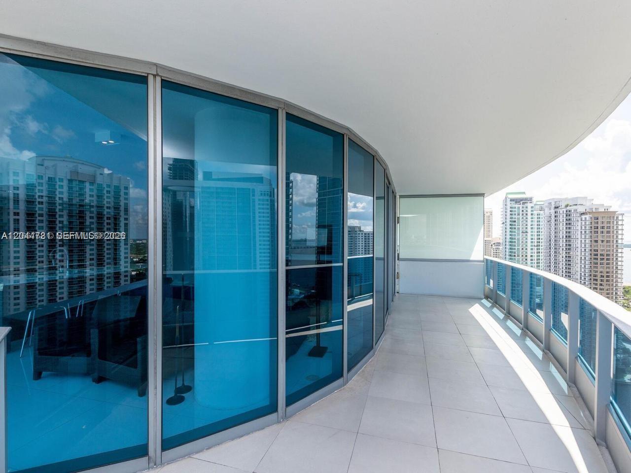A curved balcony with blue glass windows and tile flooring overlooks a city skyline — 200 Biscayne Boulevard Way # 3102, Miami FL 33131, MIAMI, FL