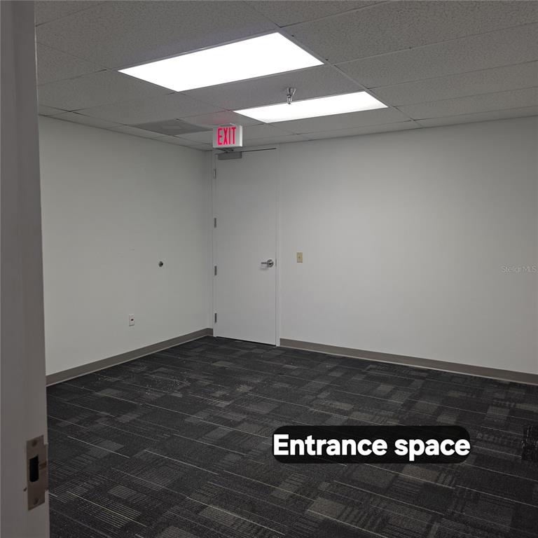 An empty office room features white walls, dark patterned carpet, and a white exit door — 29399 US HIGHWAY 19 N, CLEARWATER, FL