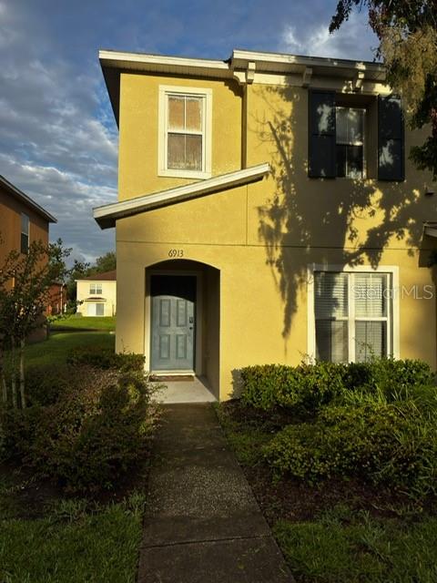 The exterior of a two-story yellow stucco house features a front door and a walkway — 6913 MARBLE FAWN PLACE, RIVERVIEW, FL