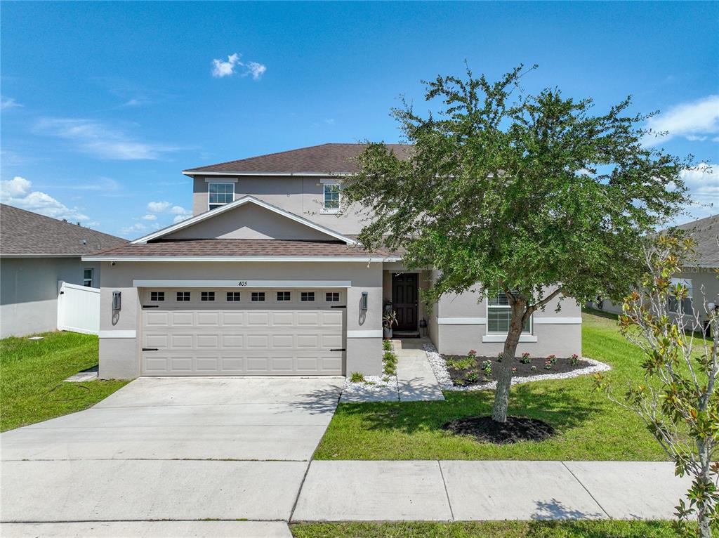 A two-story suburban house with a tan exterior, a two-car garage, and a front tree — 405 KESTREL DRIVE, GROVELAND, FL