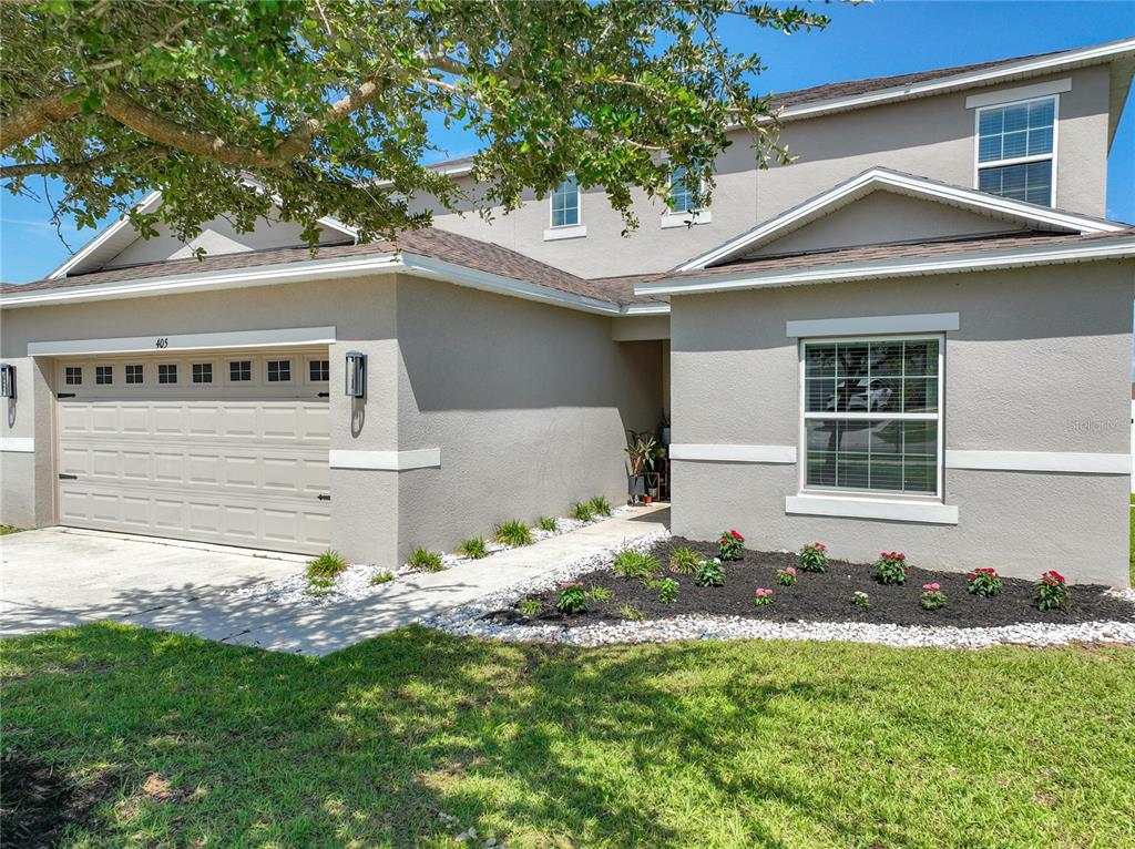 A two-story suburban house with a beige stucco exterior, a garage, and a front garden — 405 KESTREL DRIVE, GROVELAND, FL