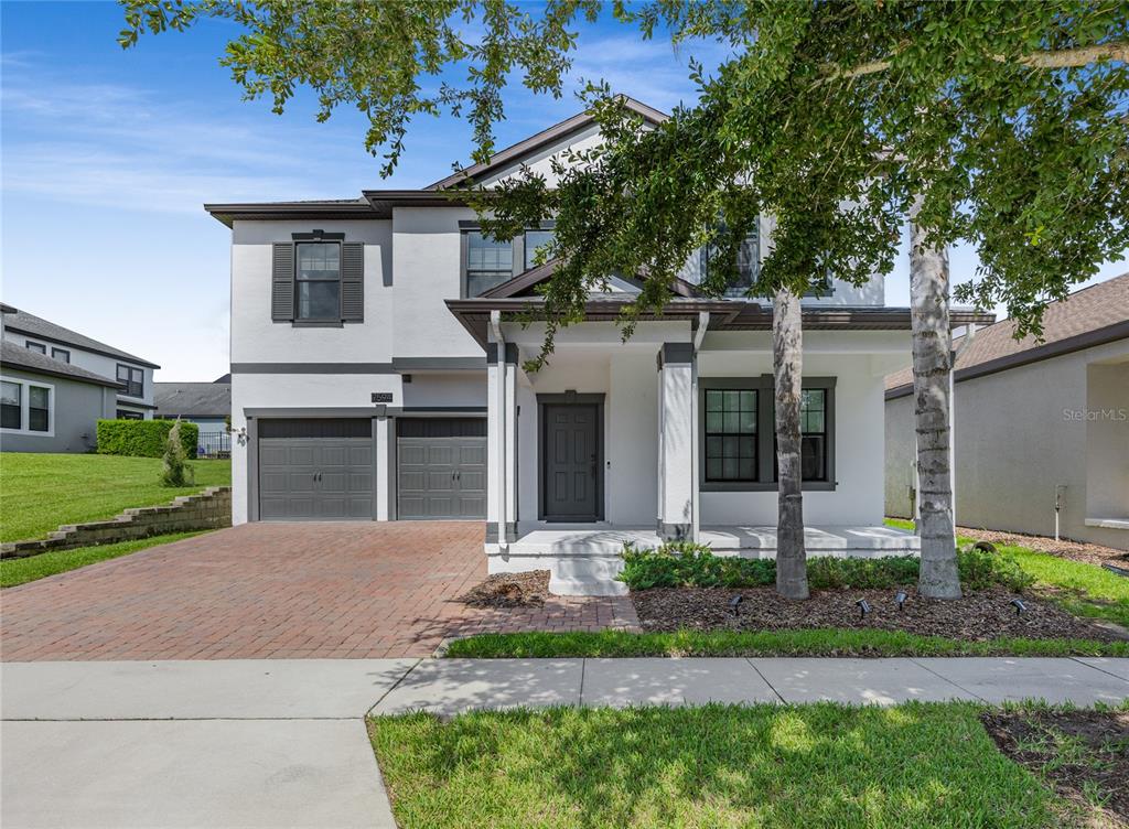 A two-story house with a brick driveway, gray garage doors, and a covered front porch — 7594 LAKE HANCOCK BOULEVARD, WINTER GARDEN, FL