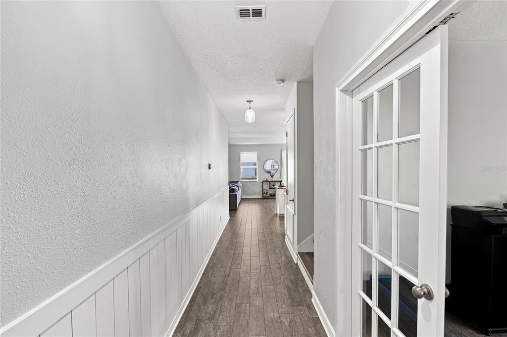 A hallway with white wainscoting and wood-look tile flooring leads toward a living area — 7594 LAKE HANCOCK BOULEVARD, WINTER GARDEN, FL