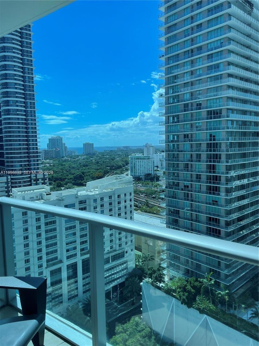 A balcony view overlooks a city skyline with tall glass skyscrapers and lush green trees — 1100 S Miami Ave # 2105, Miami FL 33130, MIAMI, FL