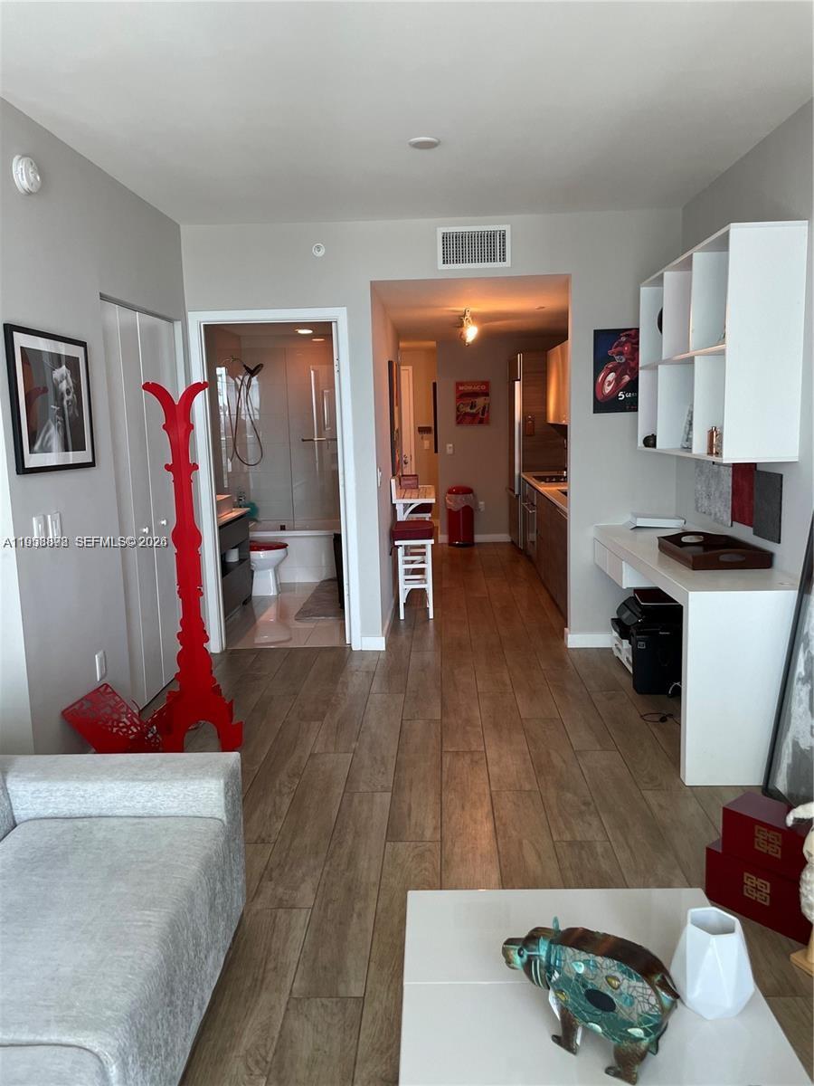 A living area with wood-look tile floors leads to a bathroom and a galley kitchen — 1100 S Miami Ave # 2105, Miami FL 33130, MIAMI, FL