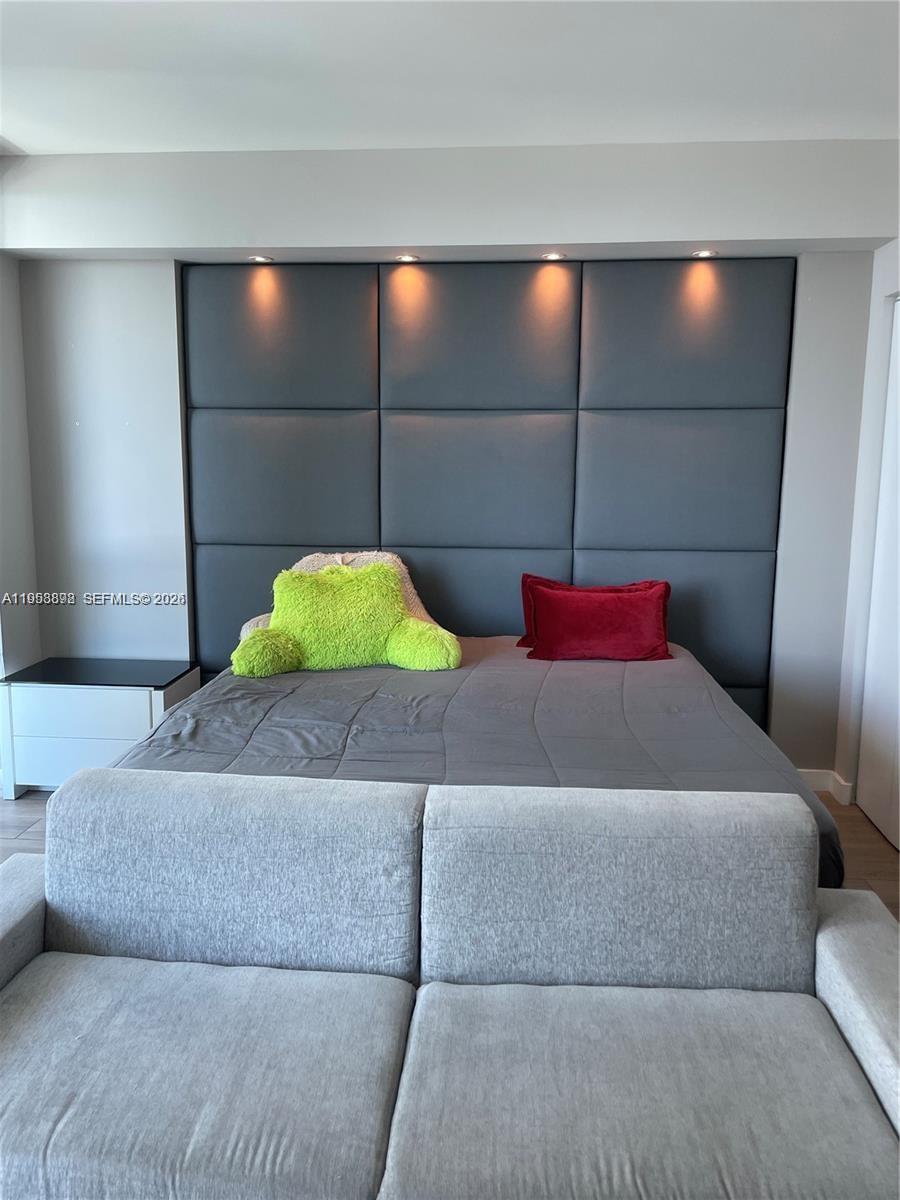 A bedroom features a gray upholstered headboard wall with recessed lighting and a sofa — 1100 S Miami Ave # 2105, Miami FL 33130, MIAMI, FL