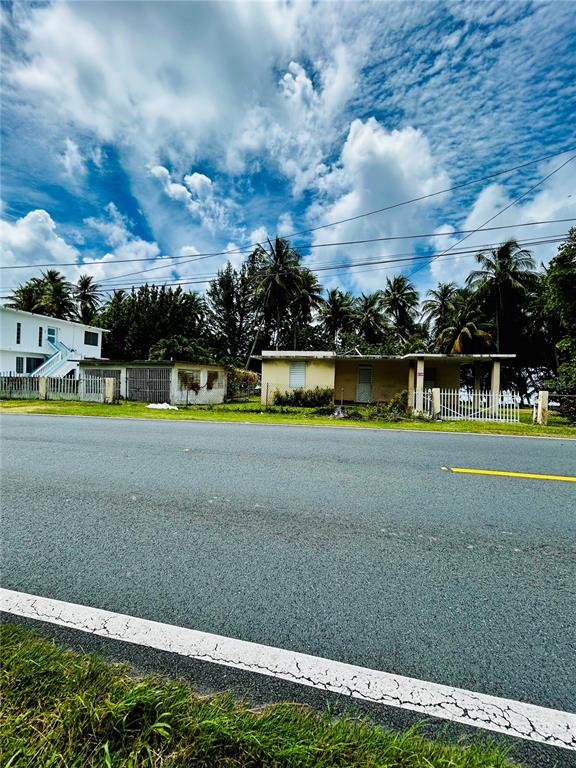 A single-story house with a flat roof sits behind a white fence near a road — KM 115.8 PR-3 GUARDARRAYAS, PATILLAS, PR