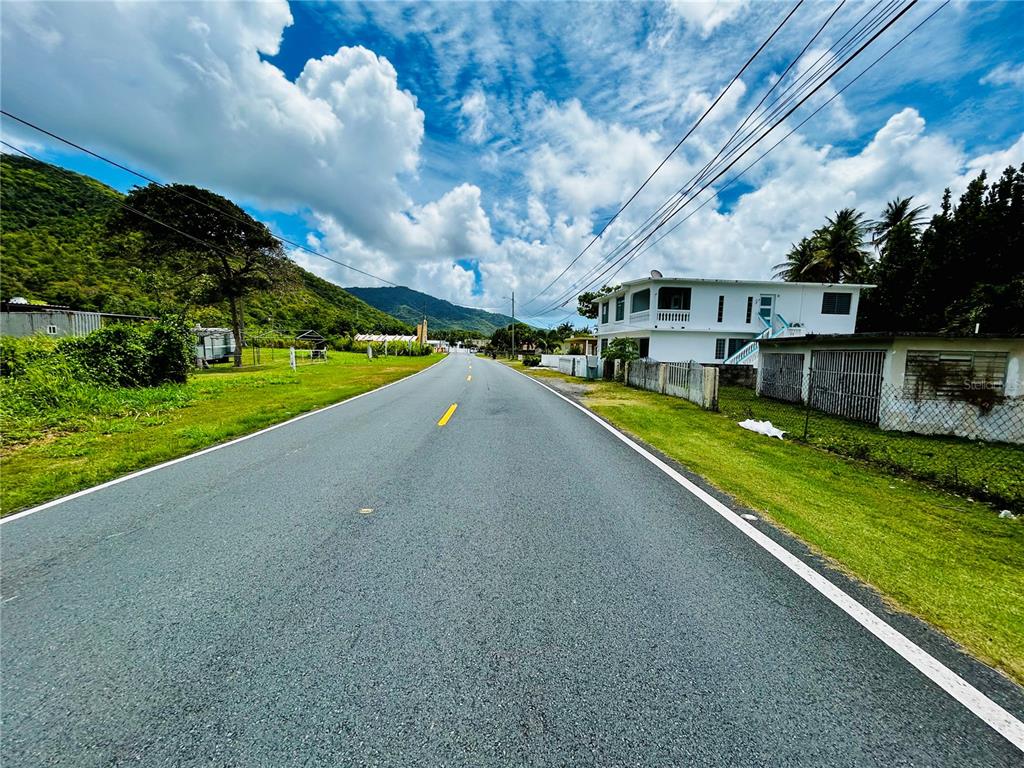 A paved road stretches toward mountains under a blue sky with a white house nearby — KM 115.8 PR-3 GUARDARRAYAS, PATILLAS, PR