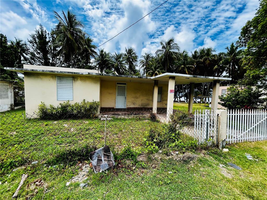 A single-story house with a flat roof and a covered porch sits behind a fence — KM 115.8 PR-3 GUARDARRAYAS, PATILLAS, PR