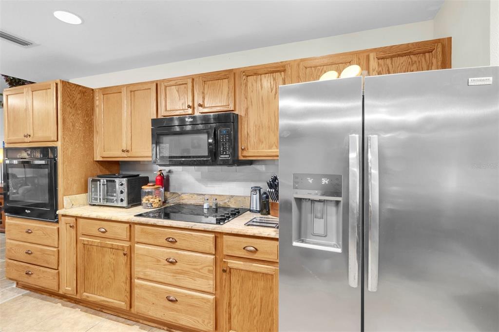 A kitchen features oak cabinets, stainless steel appliances, and a light-colored stone countertop — 11058 N MORRELL DRIVE, CITRUS SPRINGS, FL
