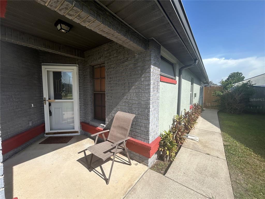 A gray brick house exterior features a covered porch, a folding chair, and a walkway — 206 HOLLYWOOD COURT N, KISSIMMEE, FL
