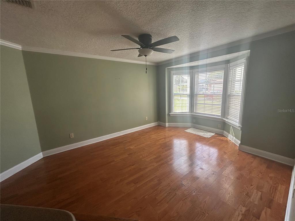 An empty room with sage green walls, hardwood floors, and a bay window — 206 HOLLYWOOD COURT N, KISSIMMEE, FL