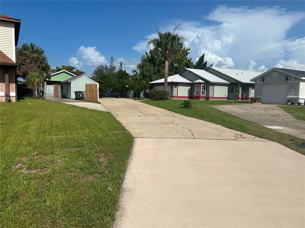 A concrete driveway leads between two houses toward a detached garage and backyard area — 206 HOLLYWOOD COURT N, KISSIMMEE, FL