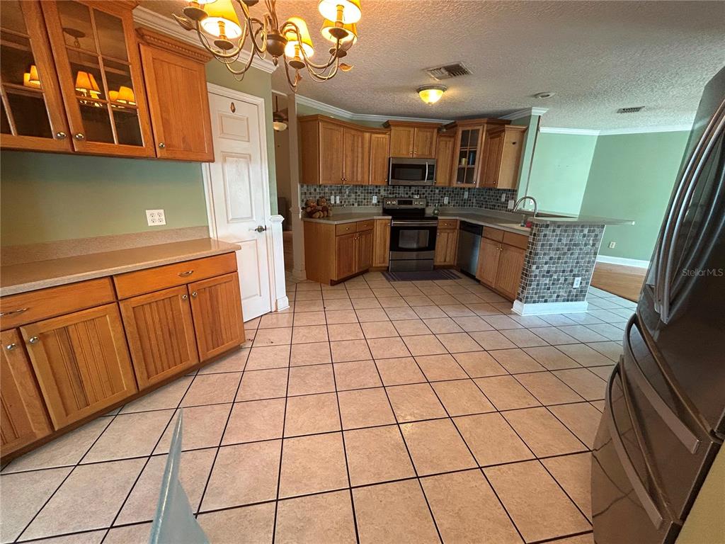 A kitchen features oak cabinets, tile flooring, stainless steel appliances, and a tiled breakfast bar — 206 HOLLYWOOD COURT N, KISSIMMEE, FL