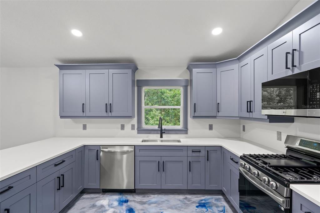 A kitchen features blue cabinets, white countertops, stainless steel appliances, and a blue-patterned floor — 478 LINCOLN AVENUE, BROOKSVILLE, FL