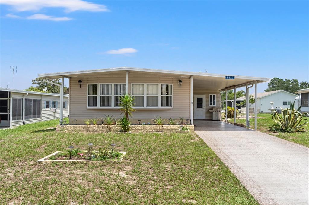 A single-story manufactured home features light siding, a front carport, and a small landscaped yard — 8427 HIGHPOINT BOULEVARD, BROOKSVILLE, FL
