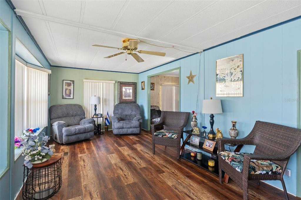 A living room features light blue walls, wood-look flooring, a ceiling fan, and various seating — 8427 HIGHPOINT BOULEVARD, BROOKSVILLE, FL