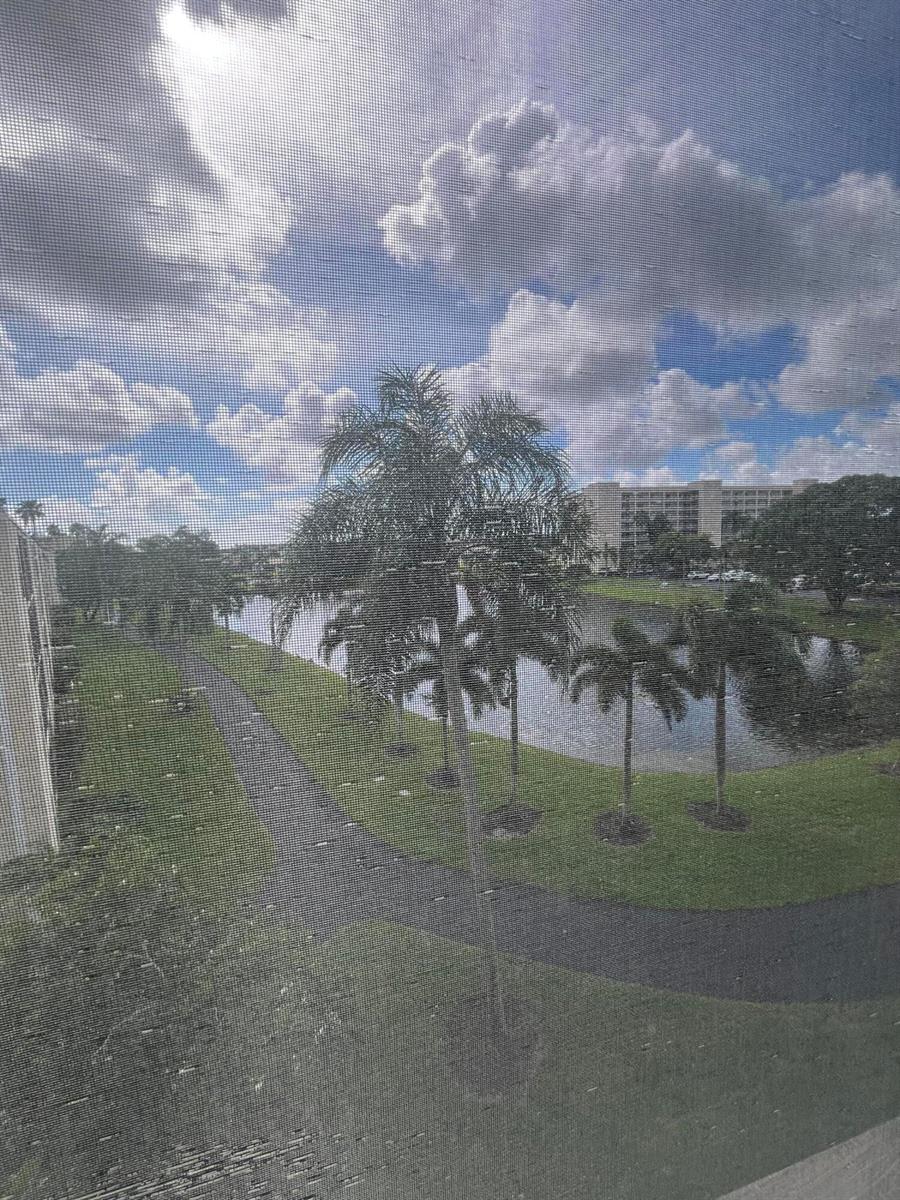 View of a pond, palm trees, and a walking path from behind a window screen — 7310 Ashford Place # 401, Delray Beach FL 33446, DELRAY BEACH, FL