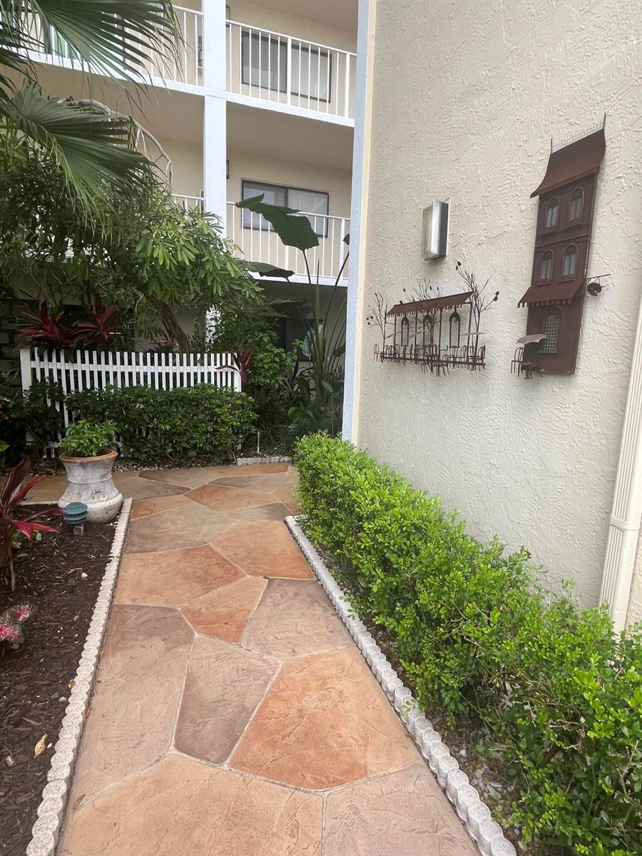A stone walkway leads toward a multi-story building with metal wall art and landscaping — 7310 Ashford Place # 401, Delray Beach FL 33446, DELRAY BEACH, FL