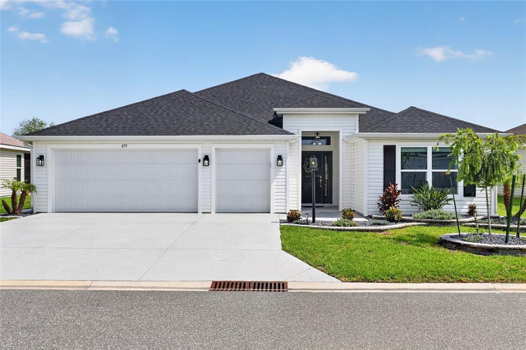 A white single-story house with a three-car garage and a landscaped front yard — 879 MORLEY AVENUE, THE VILLAGES, FL