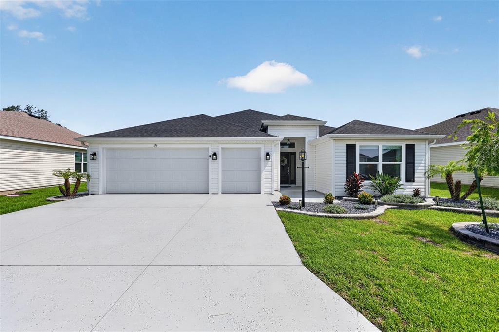 A single-story house with a white exterior, a three-car garage, and a concrete driveway — 879 MORLEY AVENUE, THE VILLAGES, FL