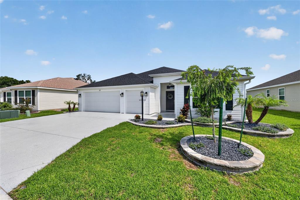 A single-story house with a white exterior, a two-car garage, and a landscaped front yard — 879 MORLEY AVENUE, THE VILLAGES, FL