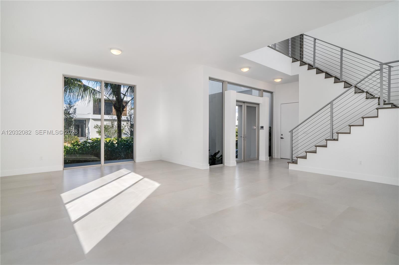 A bright, minimalist living space features large windows, white tile floors, and a metal staircase — 16720 N Botaniko Dr N, Weston FL 33326, WESTON, FL