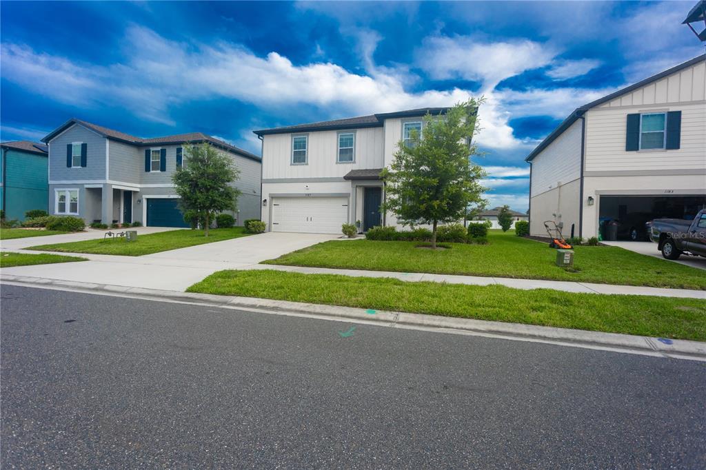 Three two-story suburban houses stand side-by-side along a paved street with green lawns — 1187 PEARL TREE ROAD, DELTONA, FL