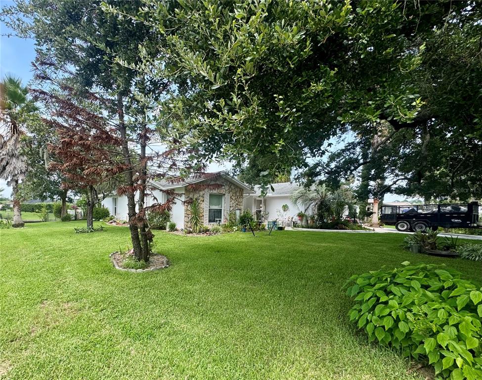 A single-story house with stone accents sits on a large, grassy lawn under mature trees — 30 FERNHAM LANE, PALM COAST, FL