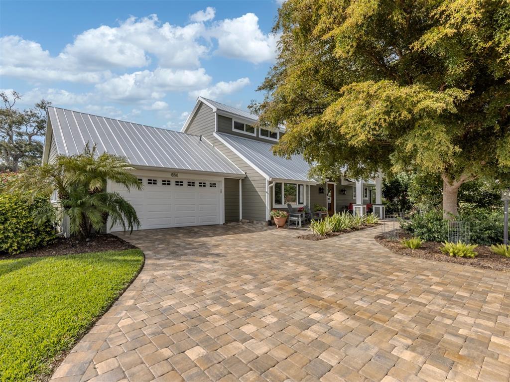 A house with a metal roof, gray siding, and a paved driveway under a large tree — 614 RAVENNA STREET, VENICE, FL