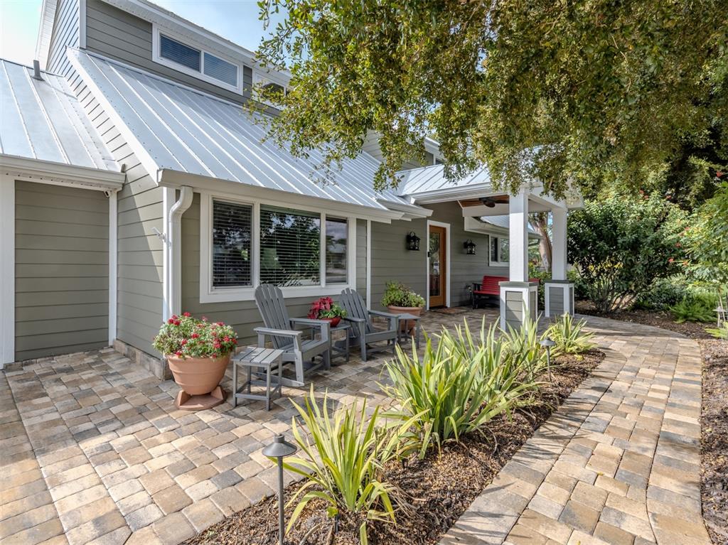 A gray house with a metal roof features a paver patio and outdoor seating area — 614 RAVENNA STREET, VENICE, FL