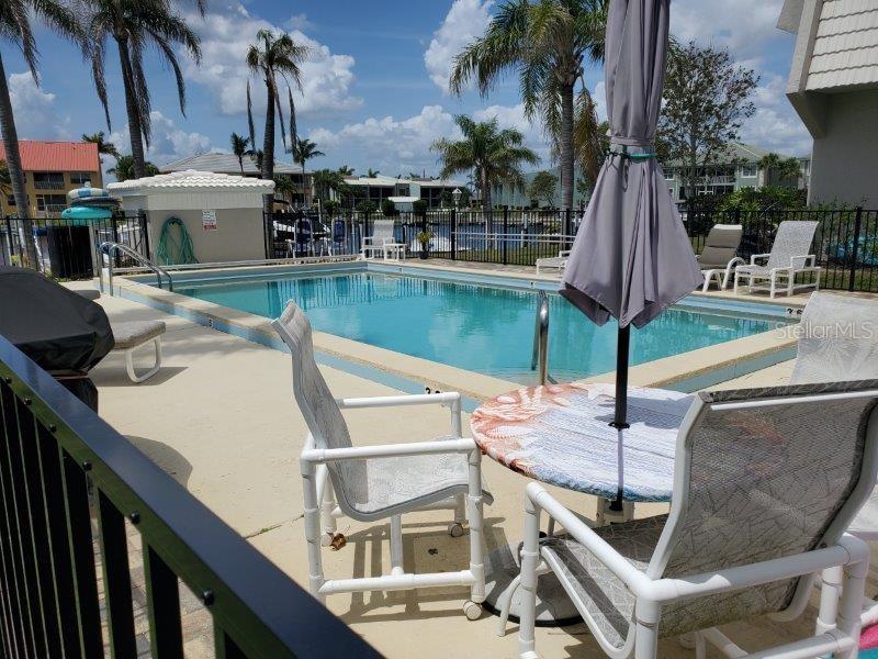 A swimming pool sits on a patio with outdoor furniture and palm trees in the background — 3233 WOOD THRUSH DRIVE UNIT 24A, PUNTA GORDA, FL
