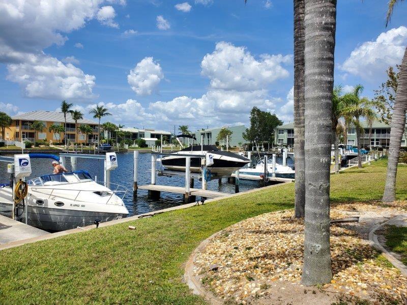 A canal view features a boat docked at a lift with residential buildings in the background — 3233 WOOD THRUSH DRIVE UNIT 24A, PUNTA GORDA, FL