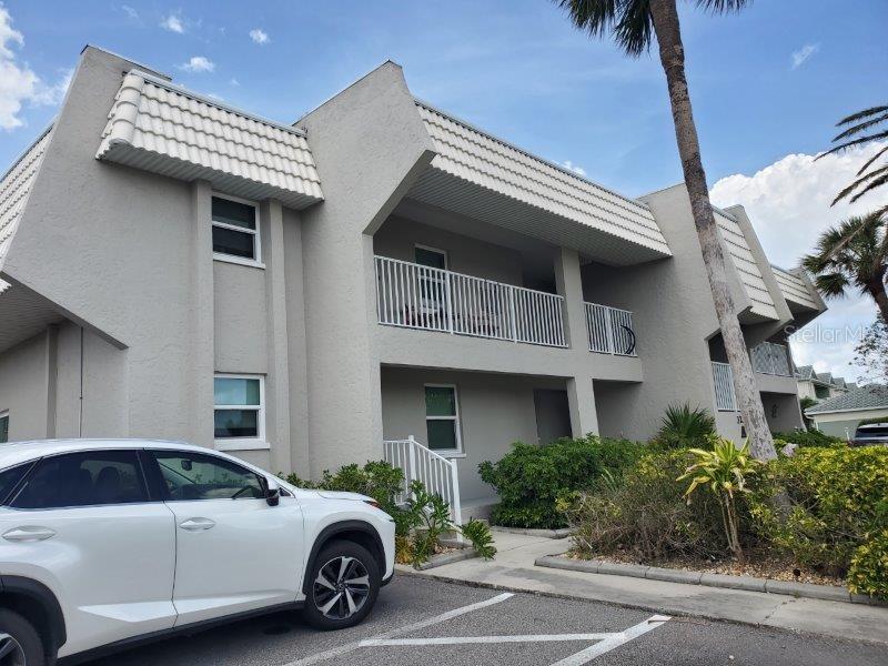 A two-story gray apartment building with white railings and a white car parked in front — 3233 WOOD THRUSH DRIVE UNIT 24A, PUNTA GORDA, FL