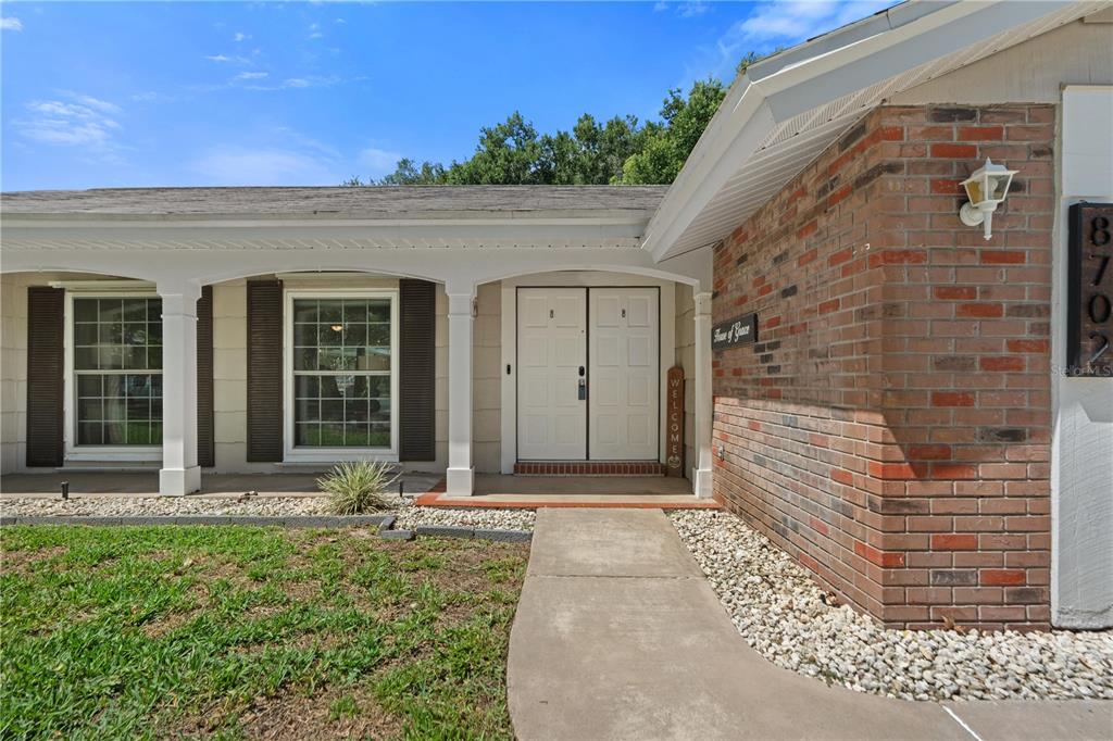 The exterior of a single-story home features a brick facade, white columns, and double doors — 8702 POWDERHORN ROW, HUDSON, FL
