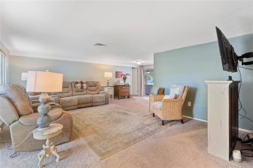 A living room features a beige sofa, a wicker chair, and a mounted television — 8702 POWDERHORN ROW, HUDSON, FL
