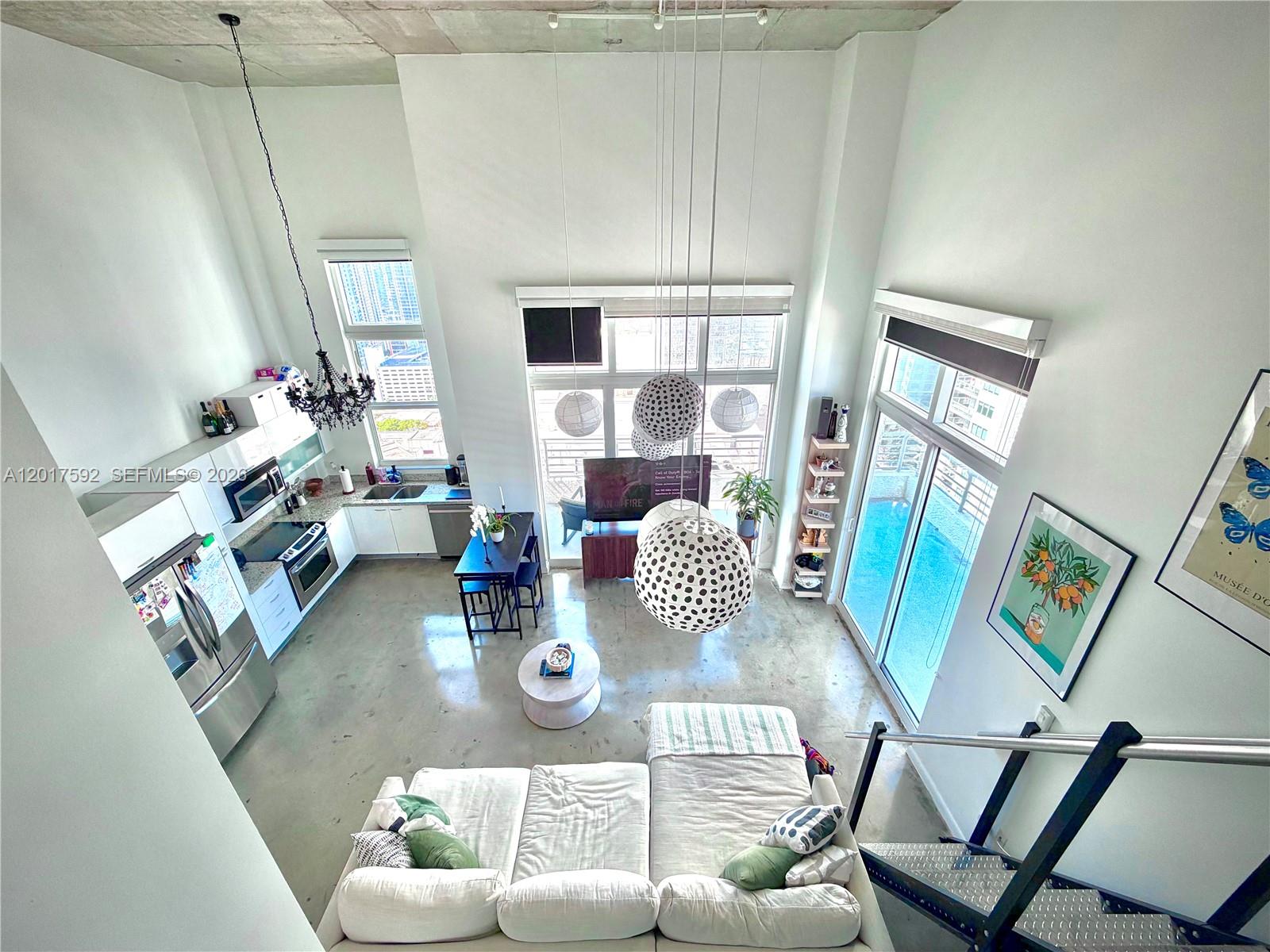 A high-angle view of a modern loft living area with concrete floors and tall windows — 133 NE 2nd Ave # 3501, Miami FL 33132, MIAMI, FL