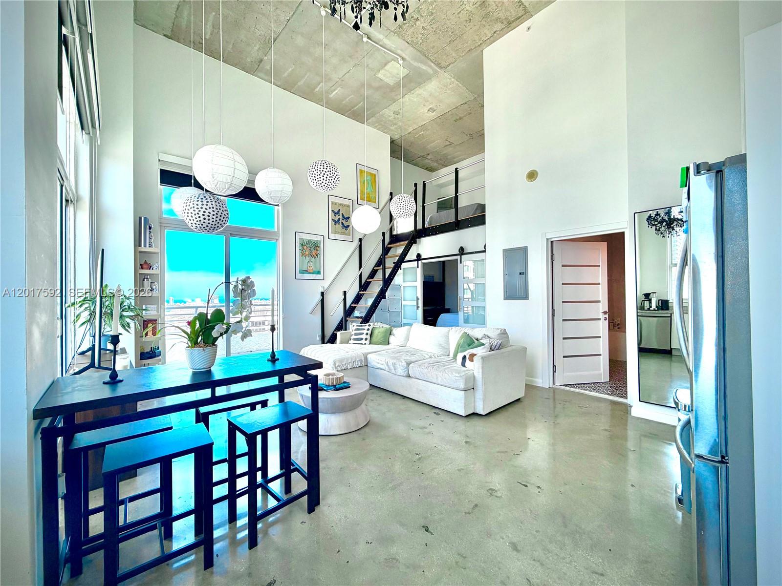 A modern loft living area features high concrete ceilings, a staircase, and a white sofa — 133 NE 2nd Ave # 3501, Miami FL 33132, MIAMI, FL