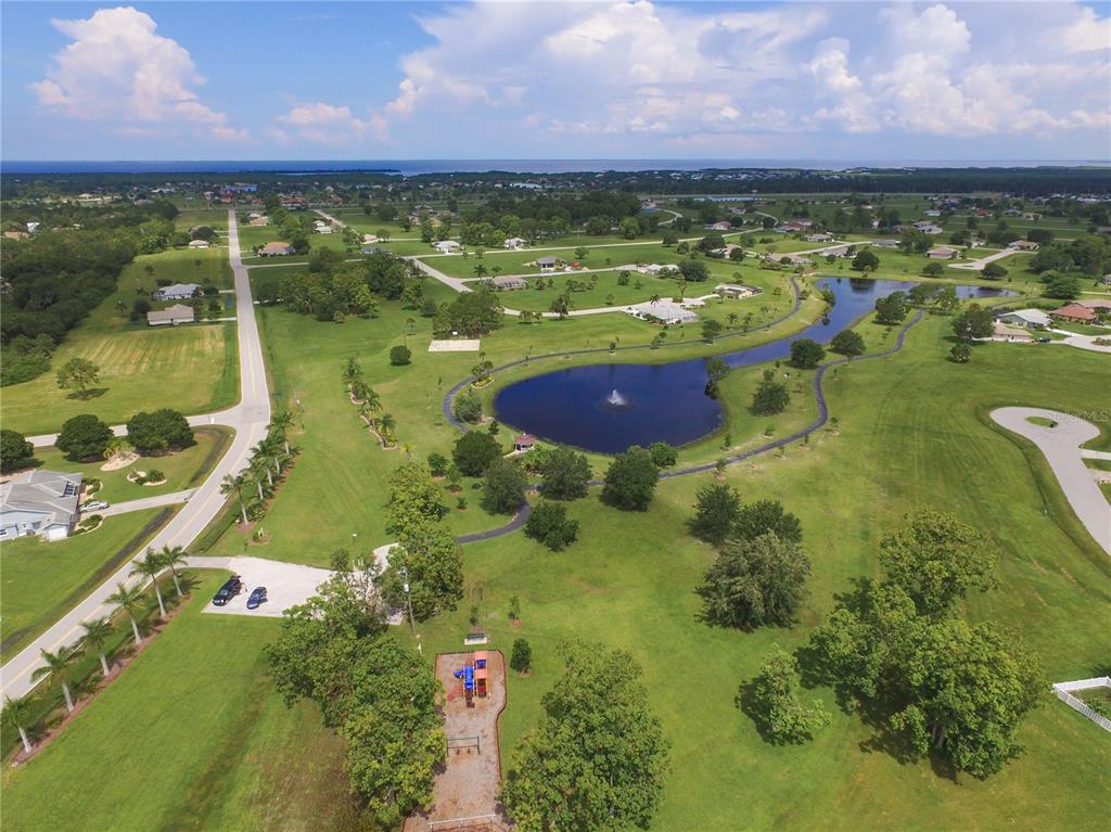 An aerial view of a residential neighborhood featuring a central pond, park, and playground — 25219 ALCAZAR DRIVE, PUNTA GORDA, FL