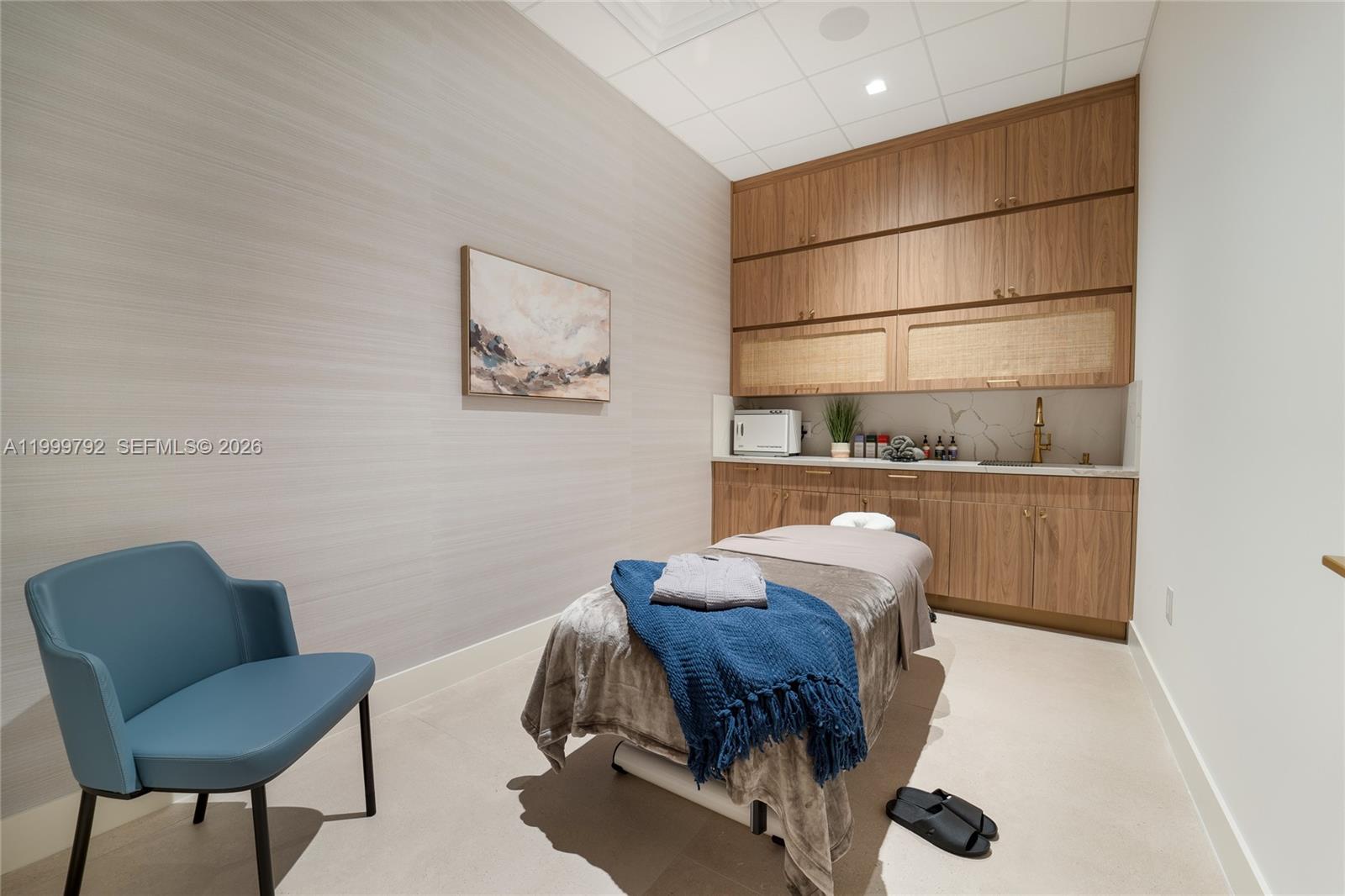 A spa treatment room features a massage table, blue chair, and wood cabinetry with a sink — 1340 S Dixie Hwy, Coral Gables FL 33146, CORAL GABLES, FL