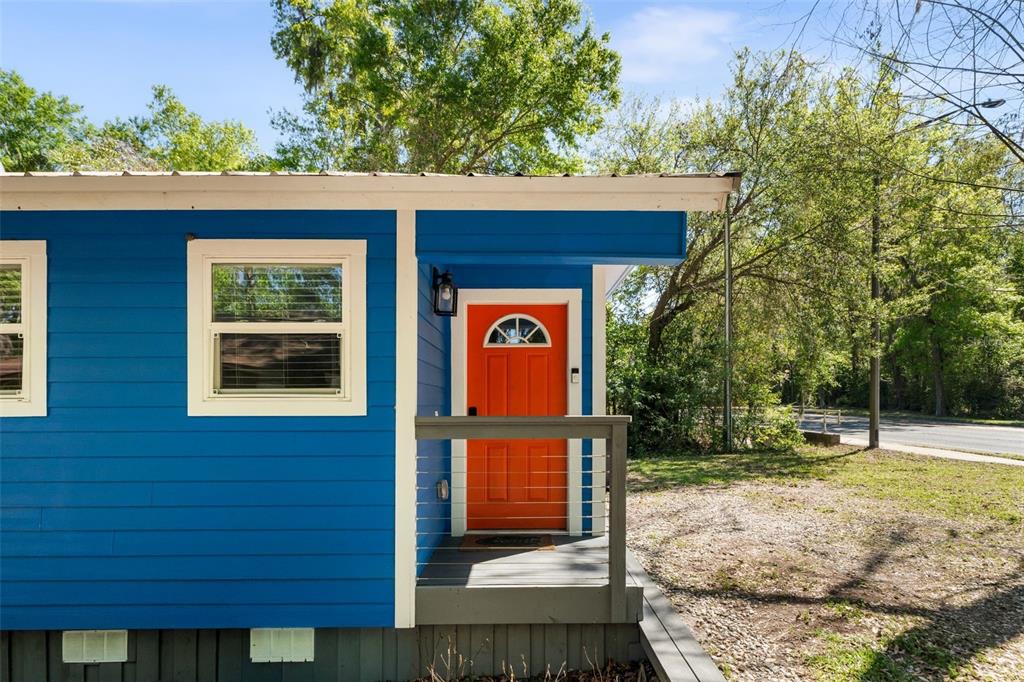 A blue house exterior features a bright orange front door and a small wooden porch — 2256 W UNIVERSITY AVENUE, GAINESVILLE, FL