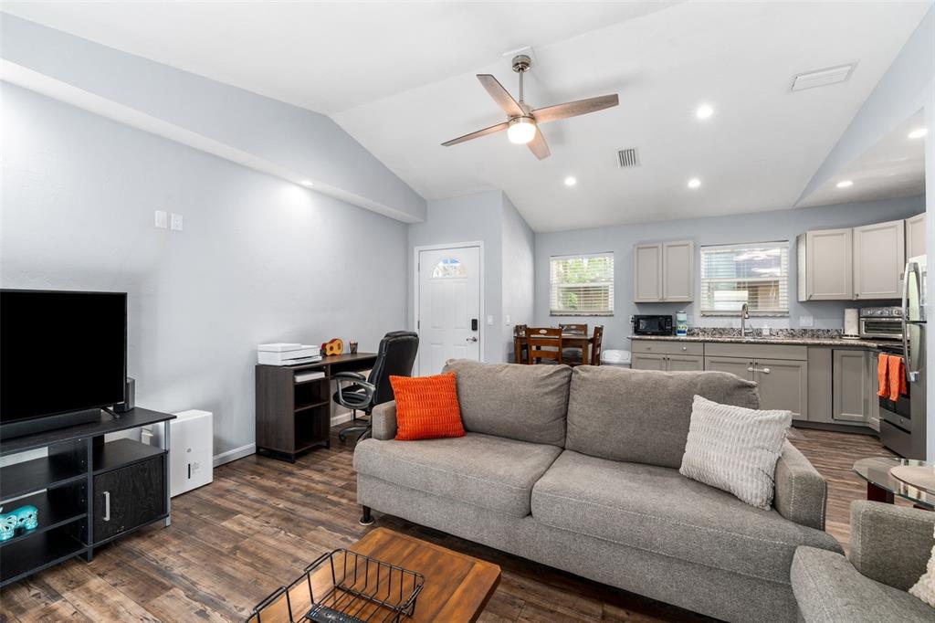A living room with a grey sofa, television, desk, and an adjacent open-concept kitchen — 2256 W UNIVERSITY AVENUE, GAINESVILLE, FL