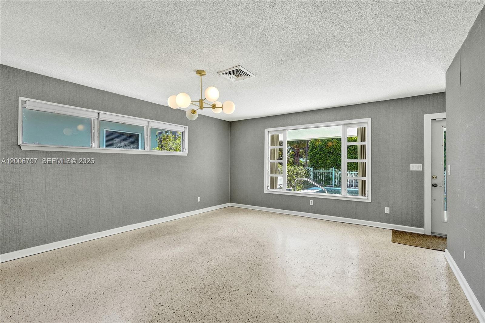 A gray-walled room features a modern chandelier, terrazzo flooring, and a view of a pool — 1421 S Palmway, Lake Worth FL 33460, LAKE WORTH, FL