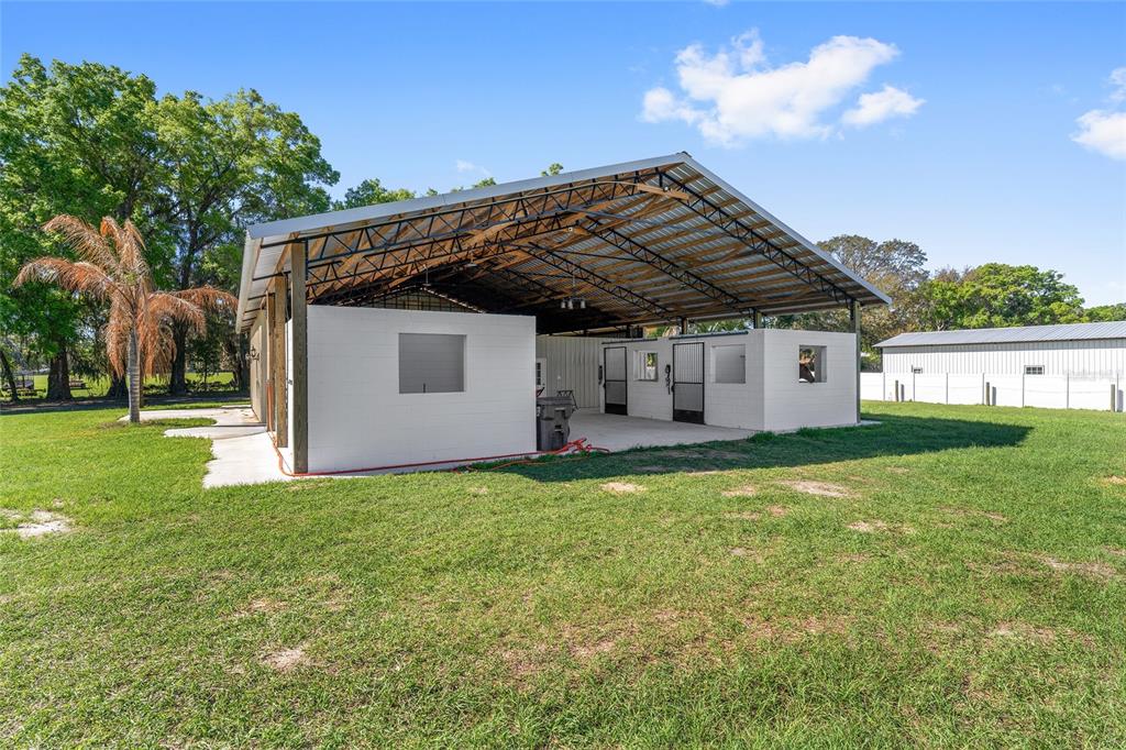 An open-air pole barn structure features white masonry walls and several horse stalls — 13869 S HWY 475, SUMMERFIELD, FL