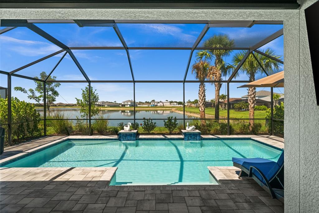 A screened-in patio features a swimming pool with water features overlooking a lake — 15620 NORTHRIDGE ROAD, PUNTA GORDA, FL