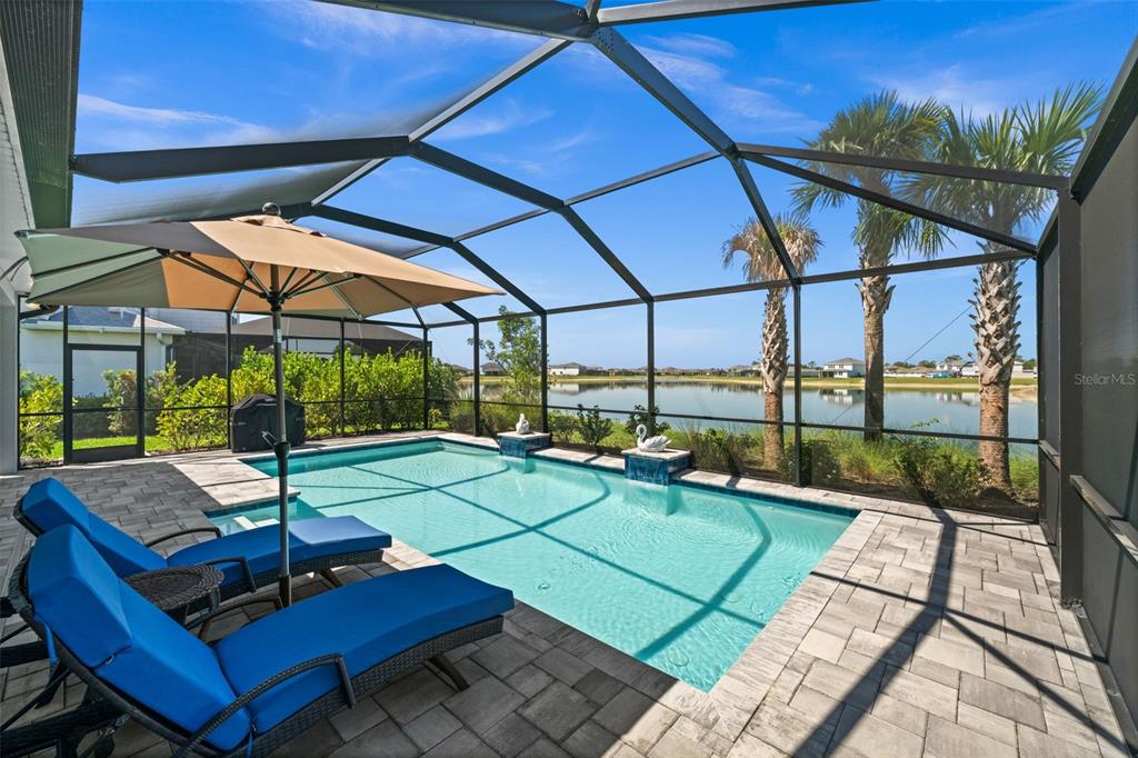 A screened-in pool patio features two blue lounge chairs, an umbrella, and a lake view — 15620 NORTHRIDGE ROAD, PUNTA GORDA, FL